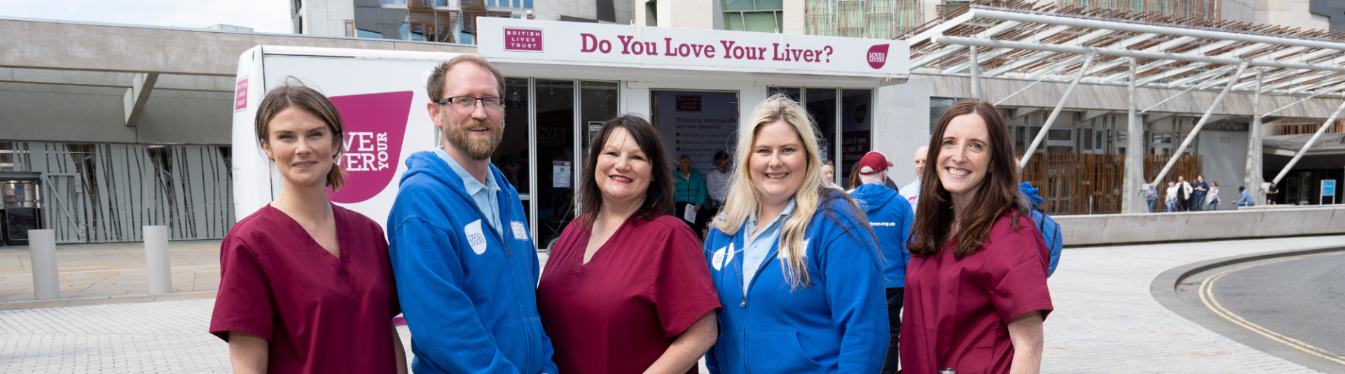 British Liver Trust Nurses and Outreach staff, dressed in red scrubs and blue hoodies, standing in front of the mobile Love Your Liver unit