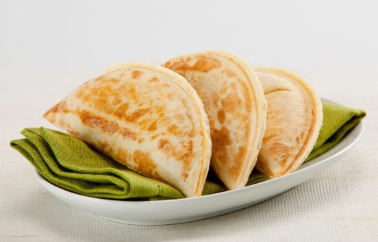 Three savoury filled pastries on an oblong white plate with a green napkin. The pastries are cooked and are a half moon shape similar to Cornish pasties or empanadas.